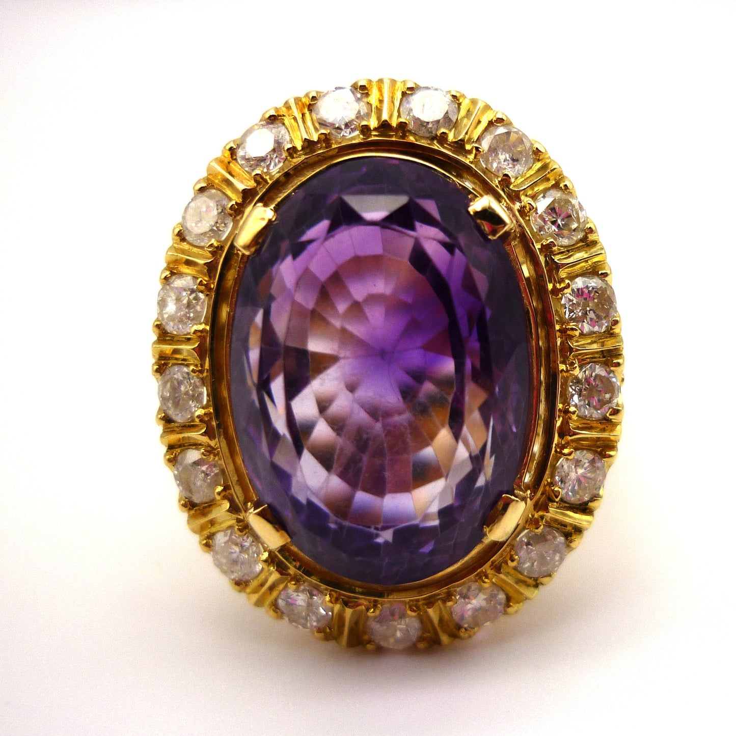 Front view of the face of a large purple amethyst ring. The central stone is faceted and surrounded by smaller diamonds set in yellow gold.