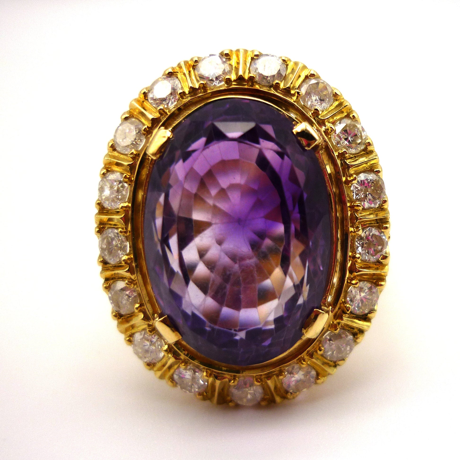 Front view of the face of a large purple amethyst ring. The central stone is faceted and surrounded by smaller diamonds set in yellow gold.