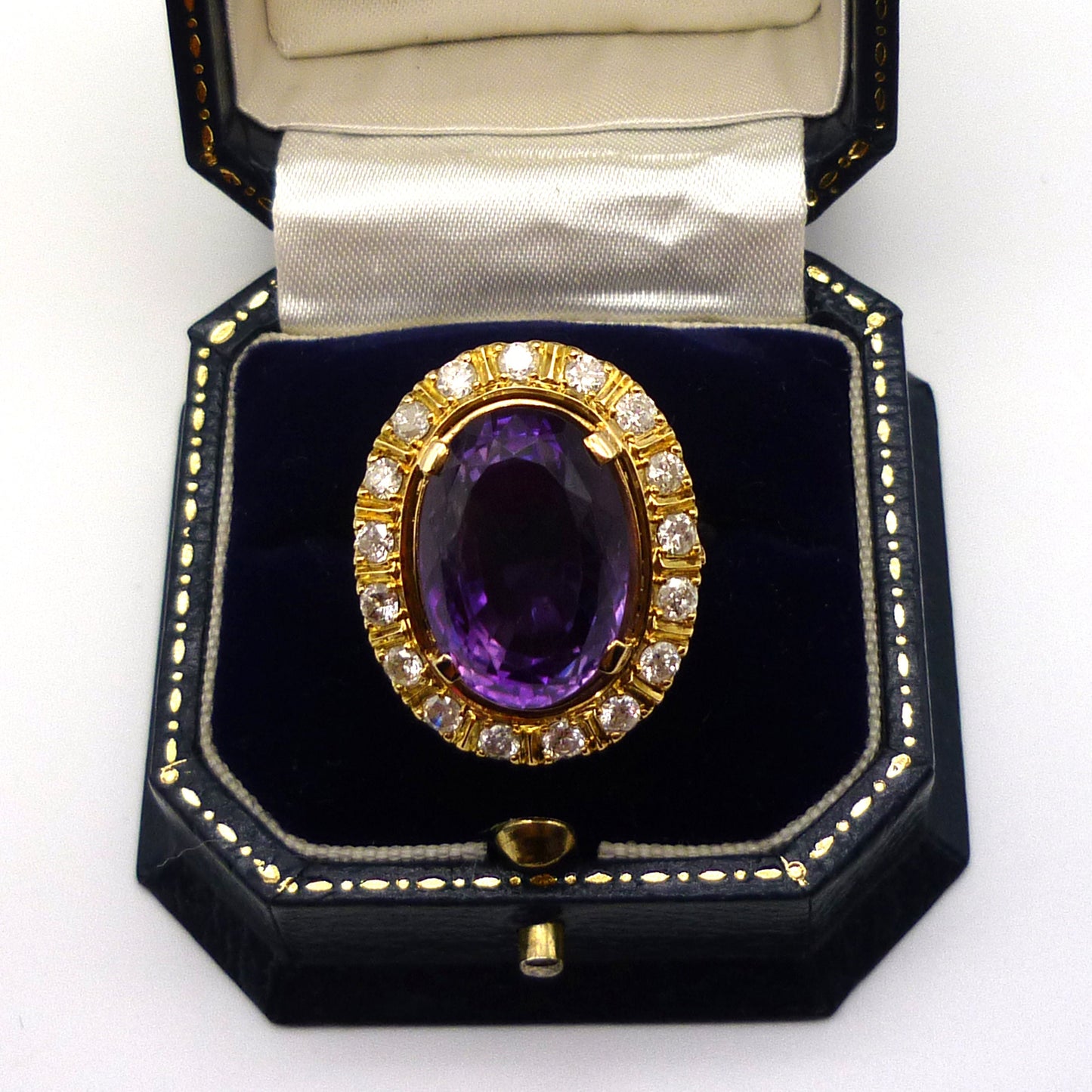 A huge purple amethyst ring with diamond and yellow gold surround in an open dark blue gift box