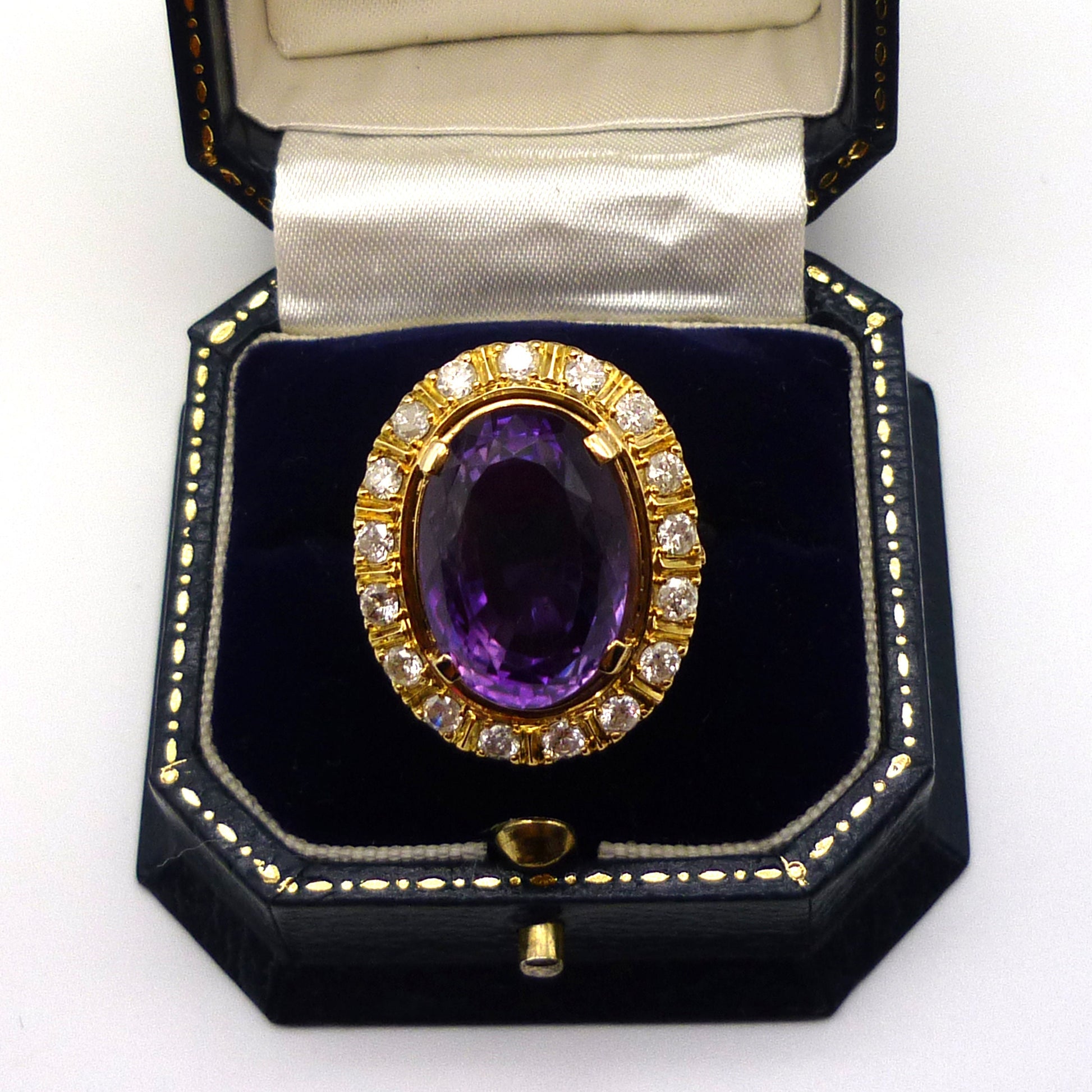 A huge purple amethyst ring with diamond and yellow gold surround in an open dark blue gift box