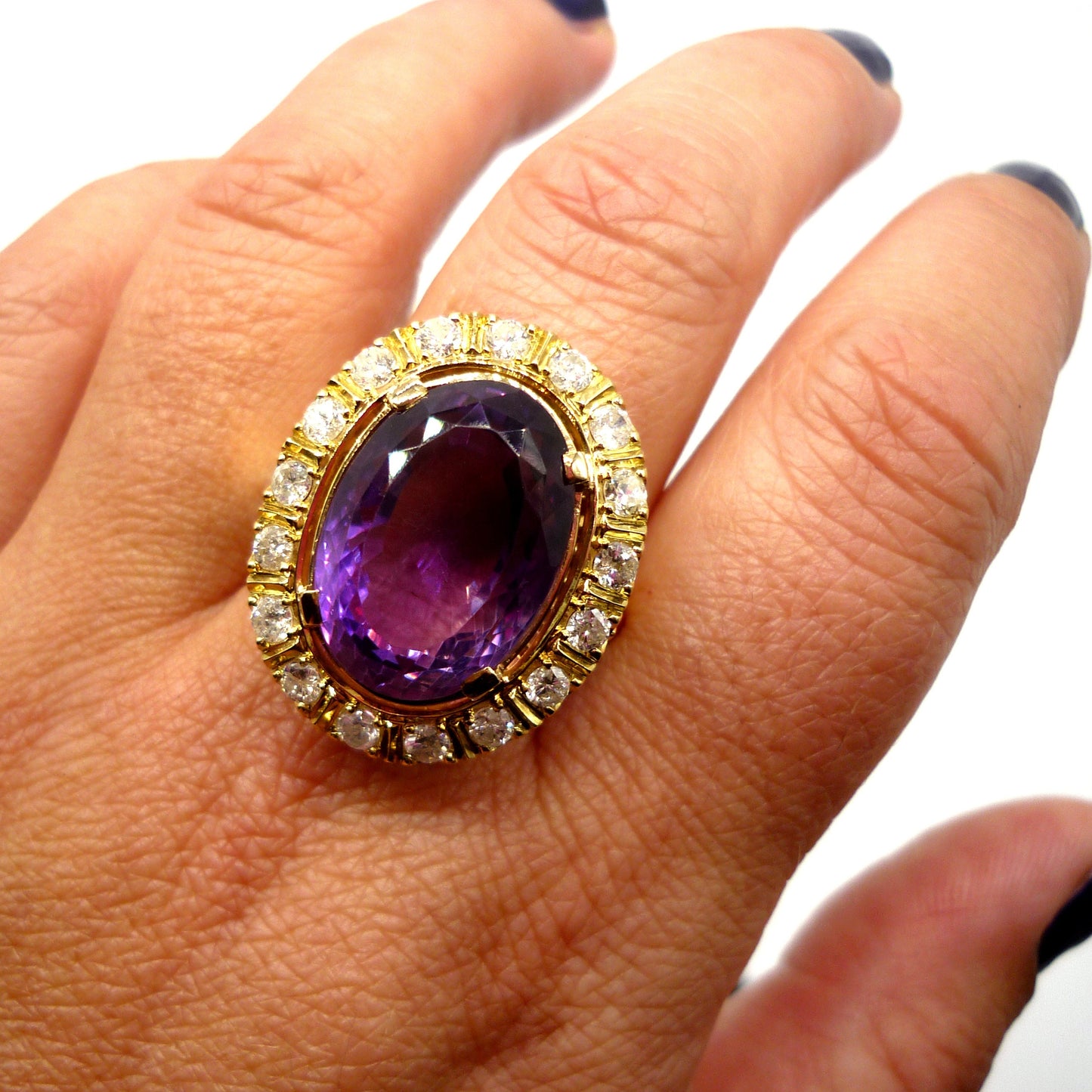 A huge purple amethyst ring with diamond and yellow gold surround on the middle finger of a woman's hand, viewed from above