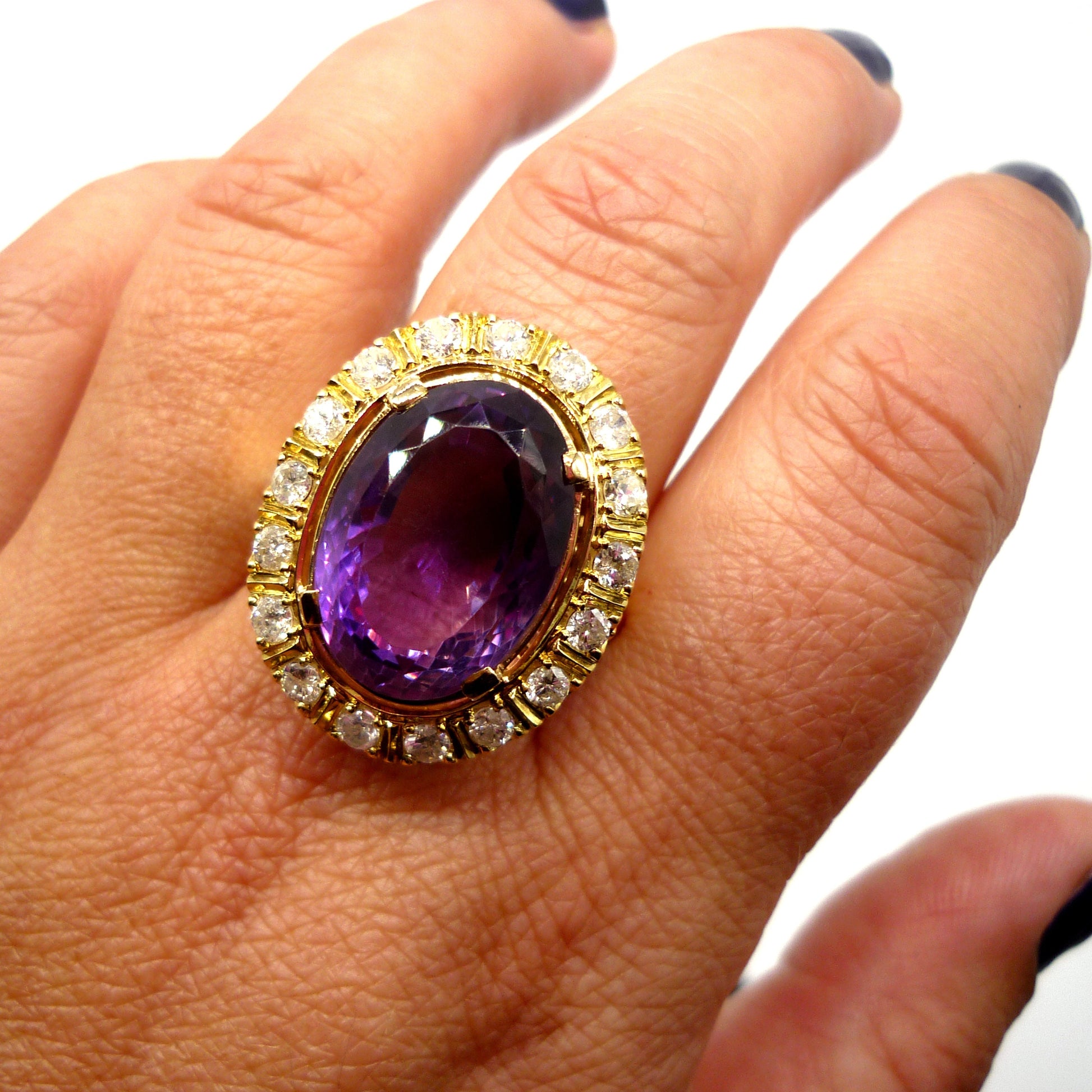 A huge purple amethyst ring with diamond and yellow gold surround on the middle finger of a woman's hand, viewed from above